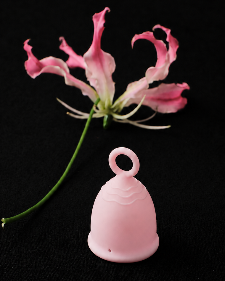 Pale pink Peachy Cup with a pink flower behind it, showing the ring stem and grip ridges