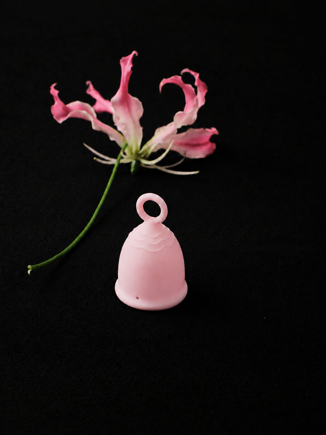 Pale pink Peachy Cup with a pink flower behind it, showing the ring stem and grip ridges