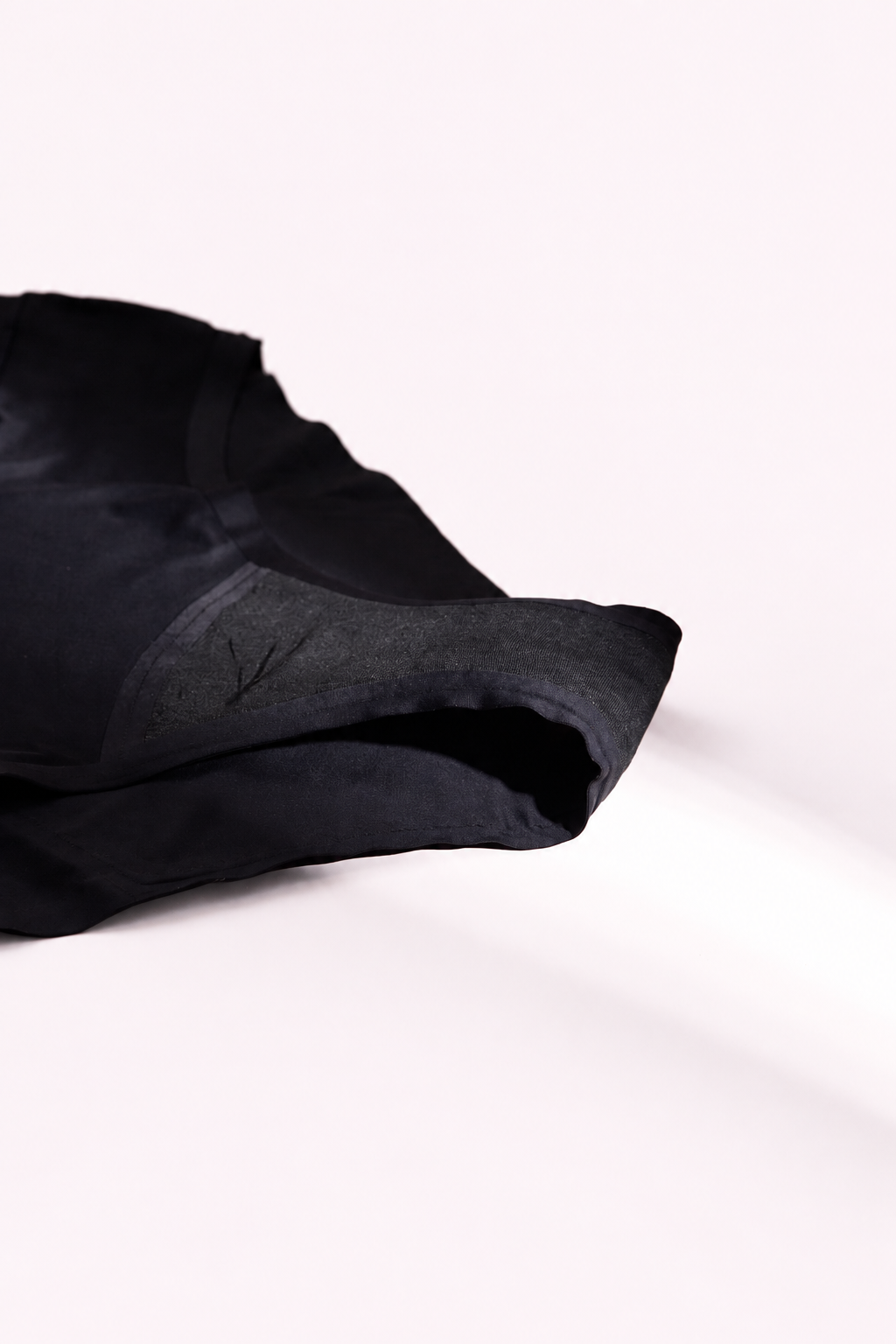 Black high-waist gusset close-up on a pale blush background